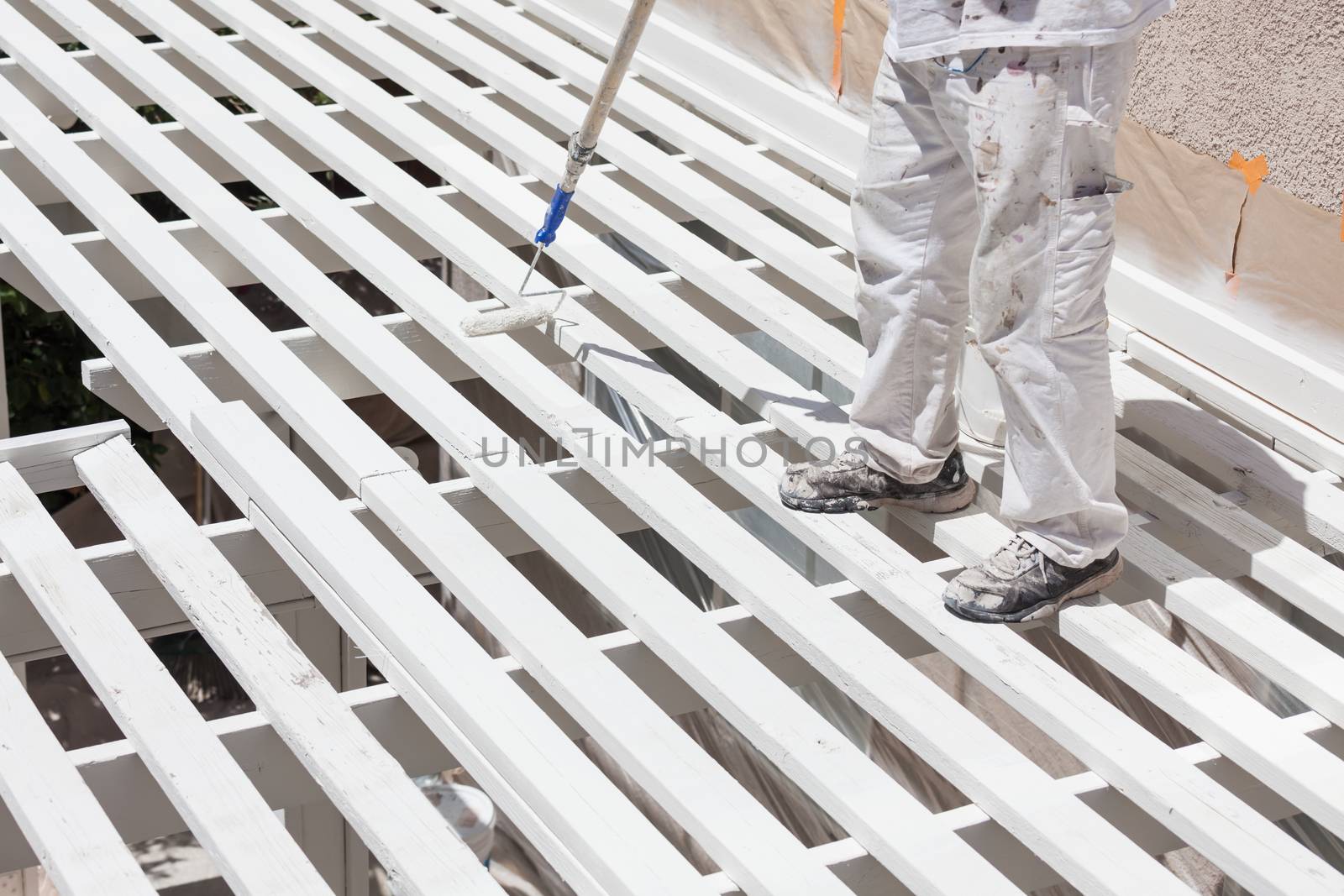 Professional Painter Rolling White Paint Onto The Top of A Home Patio Cover.