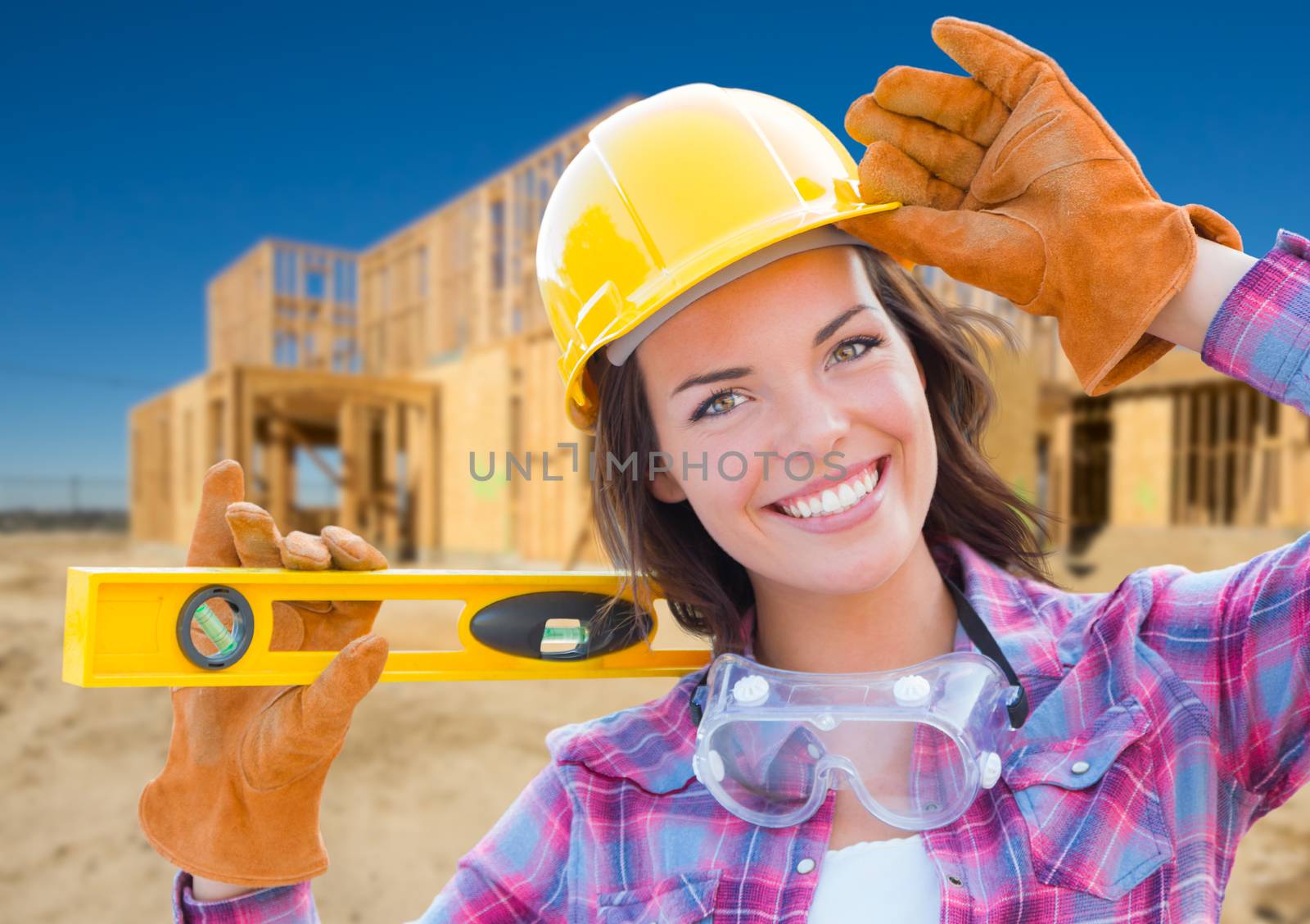 Female Construction Worker Holding Level Wearing Gloves, Hard Hat and Protective Goggles at Construction Site.