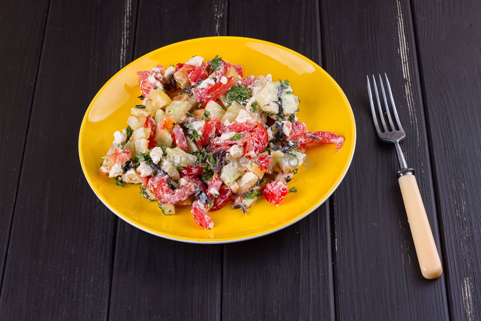 Salad of tomato pepper feta in a yellow plate on a black wooden background