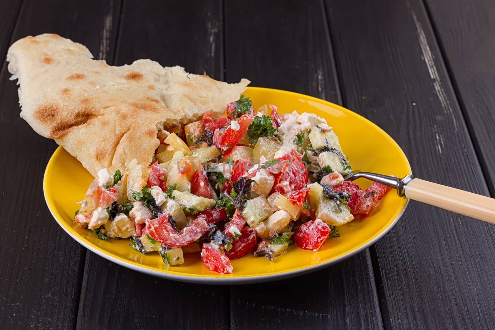 Salad of tomato pepper feta in a yellow plate on a black wooden background