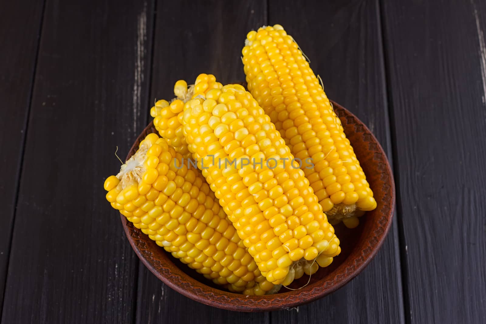 Boiled corn in a bowl on a black wooden background