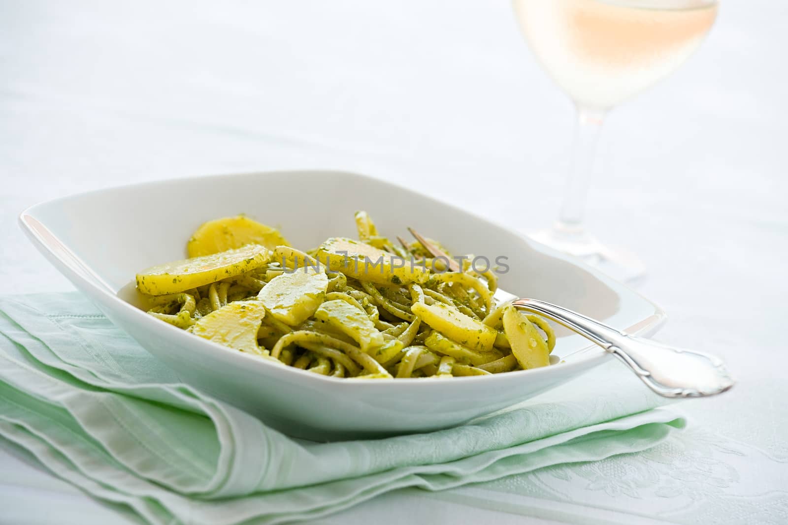 Linguine pasta with pesto genovese and potatoes over a table with fork and white wine glass