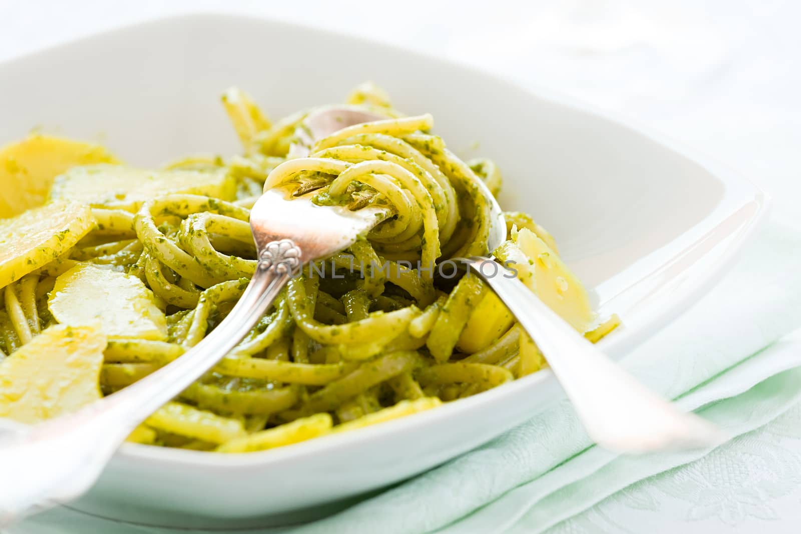 Closeup of linguine pasta with pesto genovese and potatoes over a table with cutlery