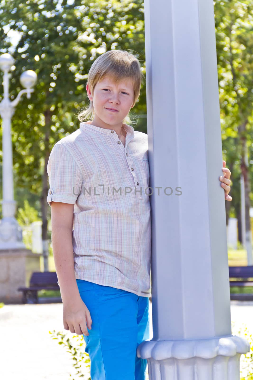 Blond boy near pole in blue trousers playing summer time