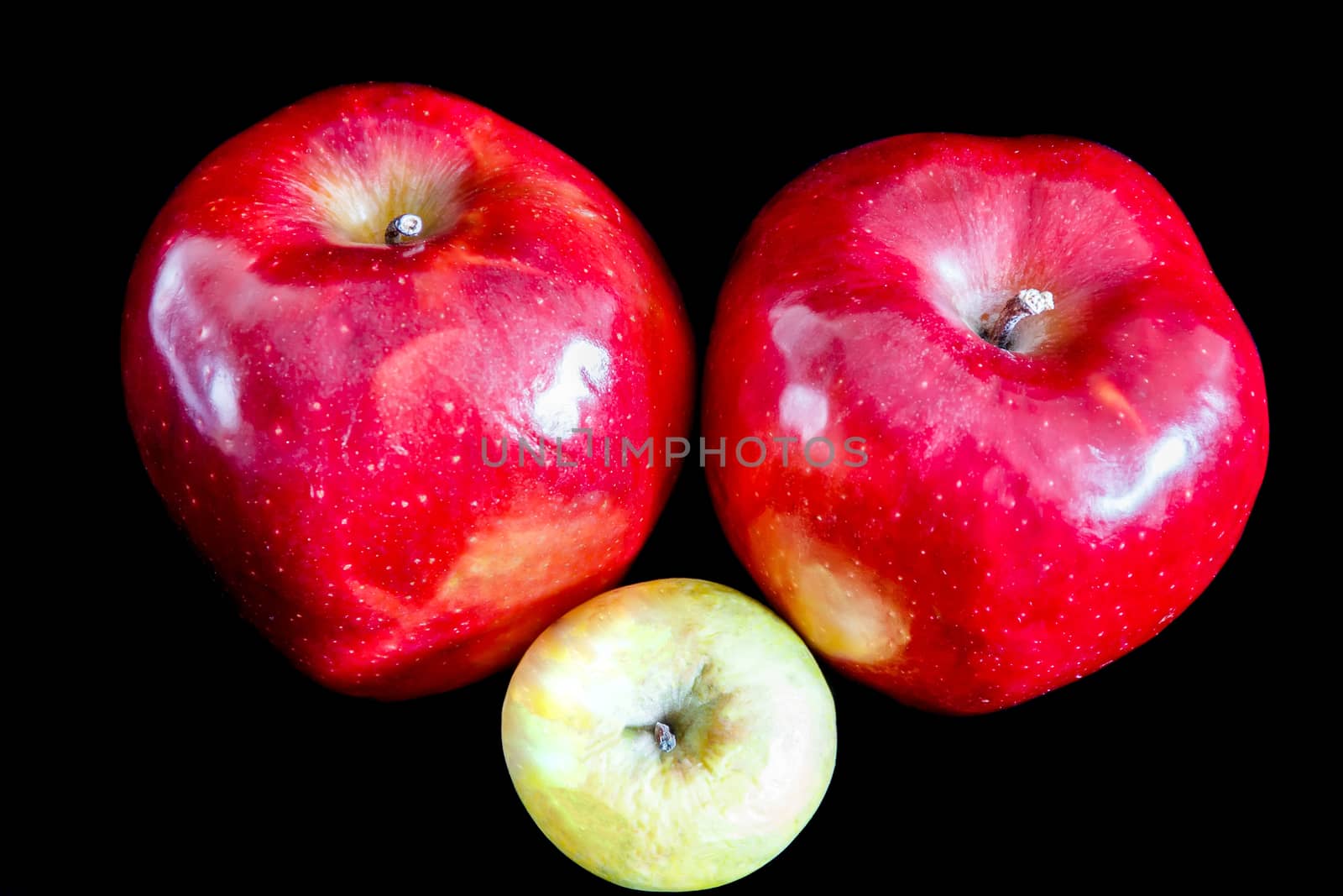 Two big red ripe appetizing apples on black background and one wrinkled green