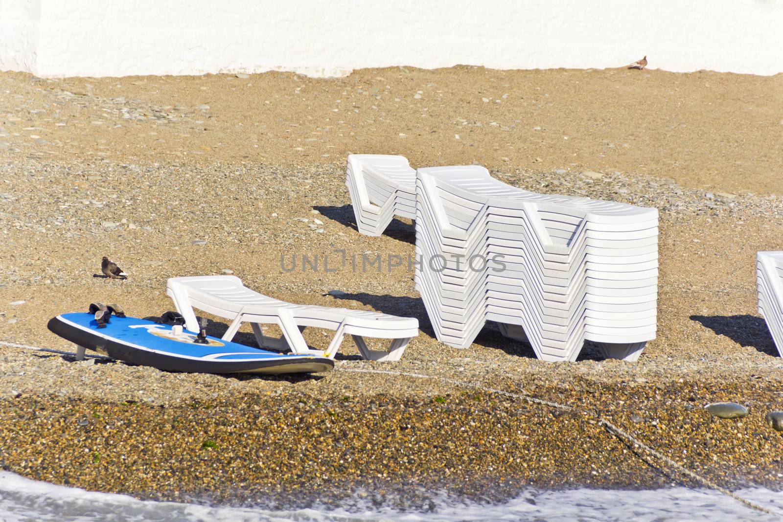 Empty beach with sun loungers and surfboard in summer day