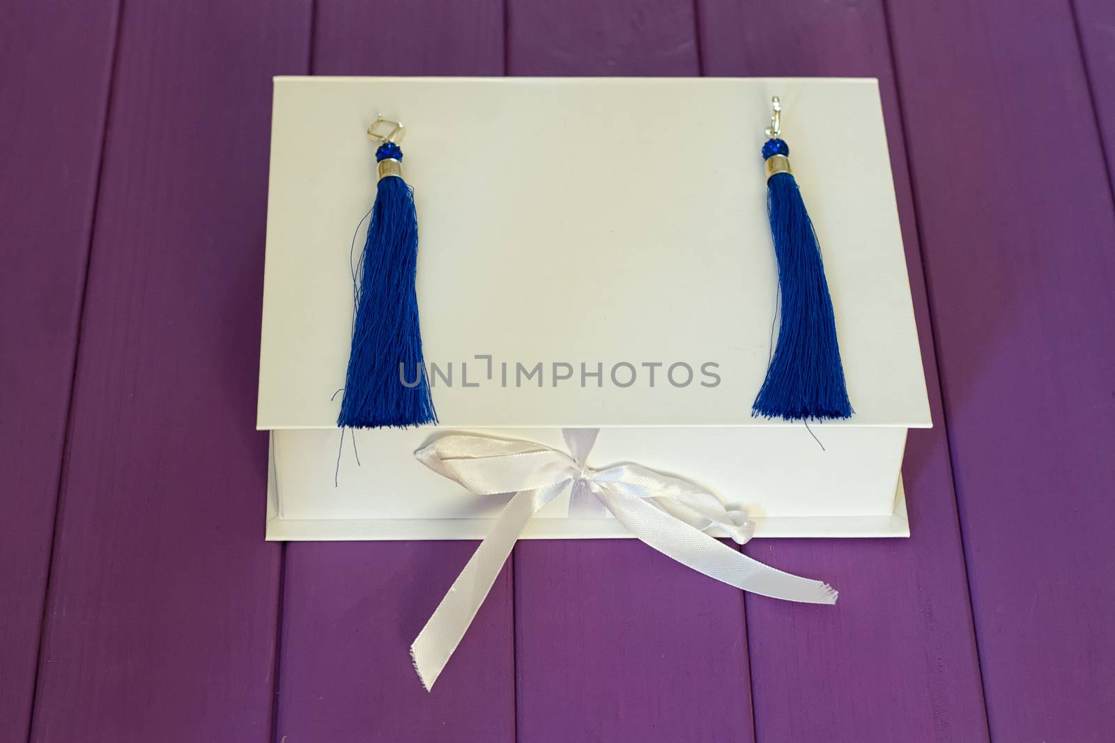 Handmade blue threaded earrings and a white box on a purple wooden background