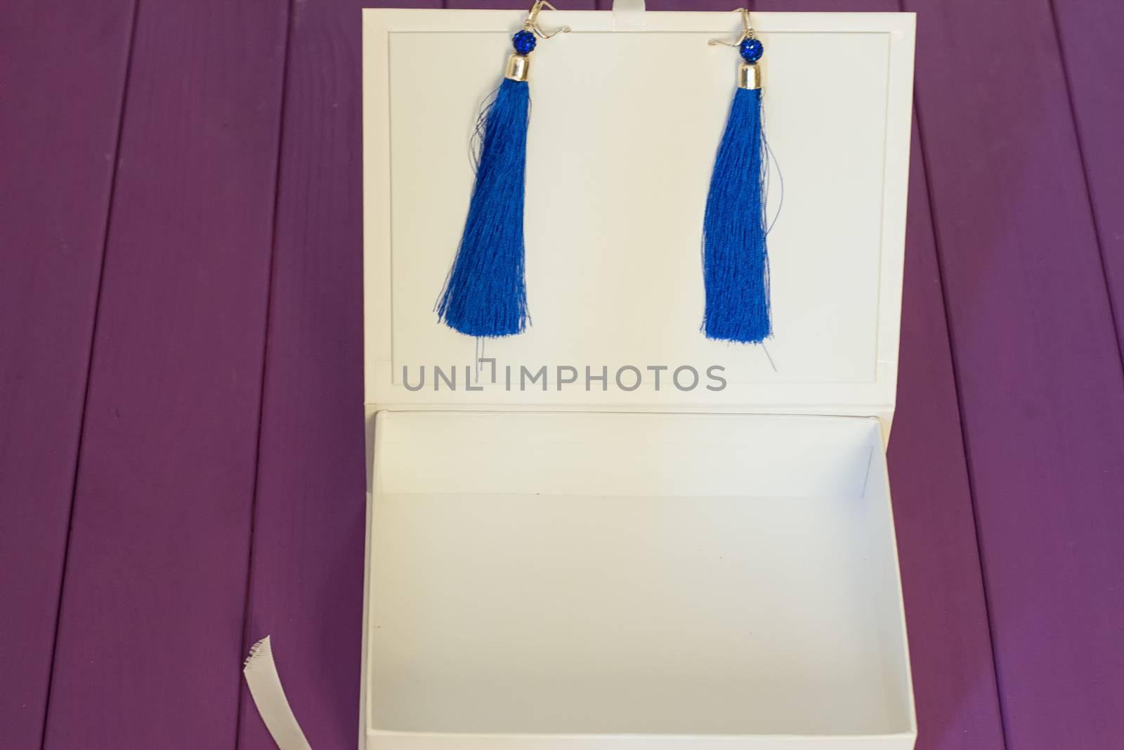 Handmade blue threaded earrings and a white box on a purple wooden background