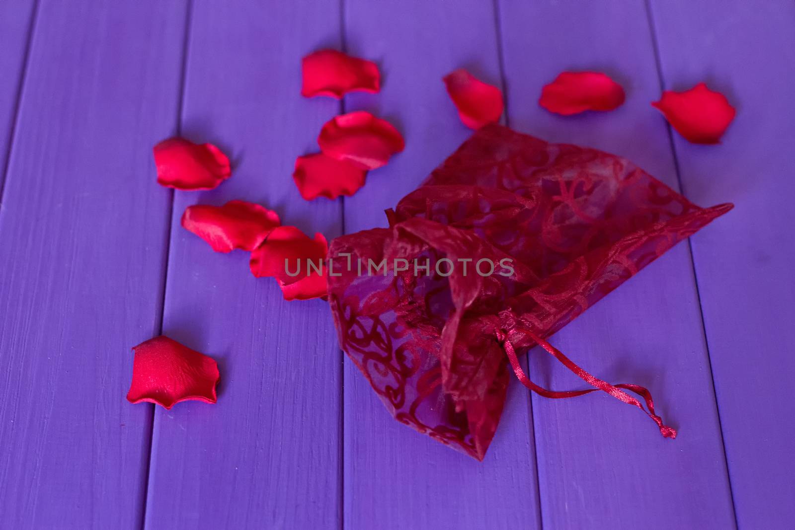 An organza pouch and petals on a purple wooden background