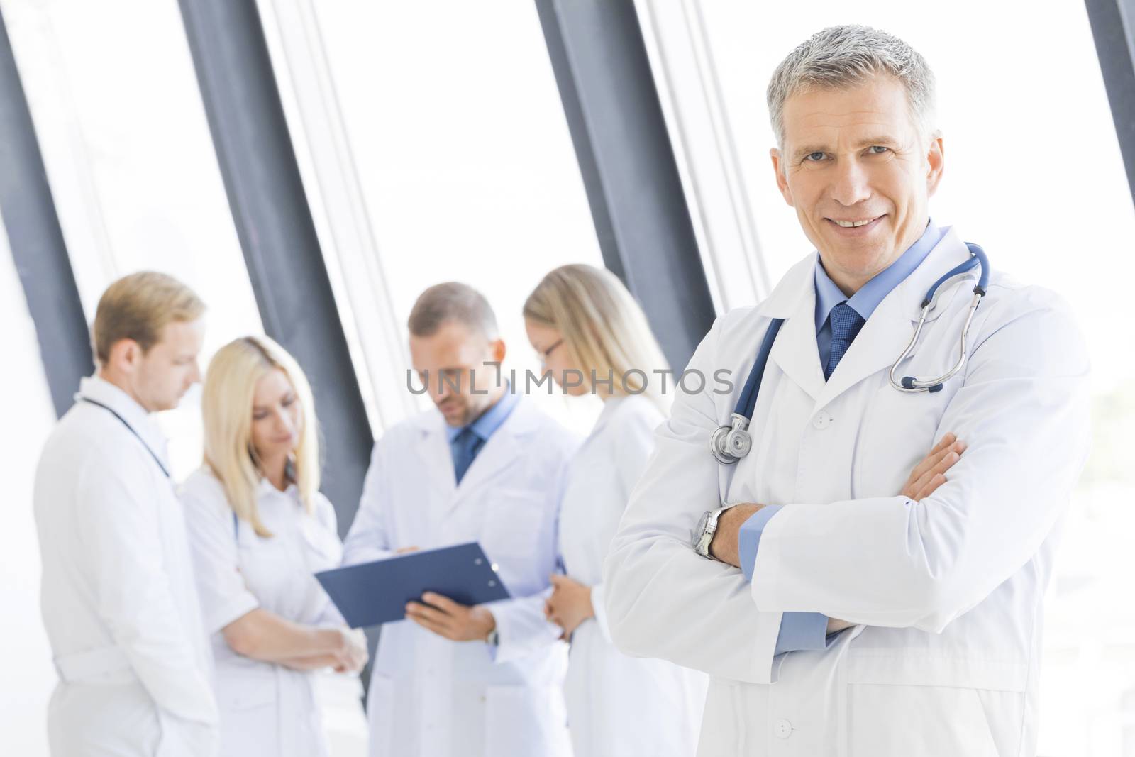 Successful mature male doctor and his team on background in clinical office