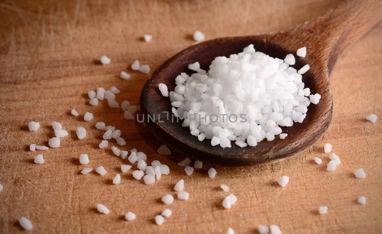 White clear salt crystals on a wooden spoon.