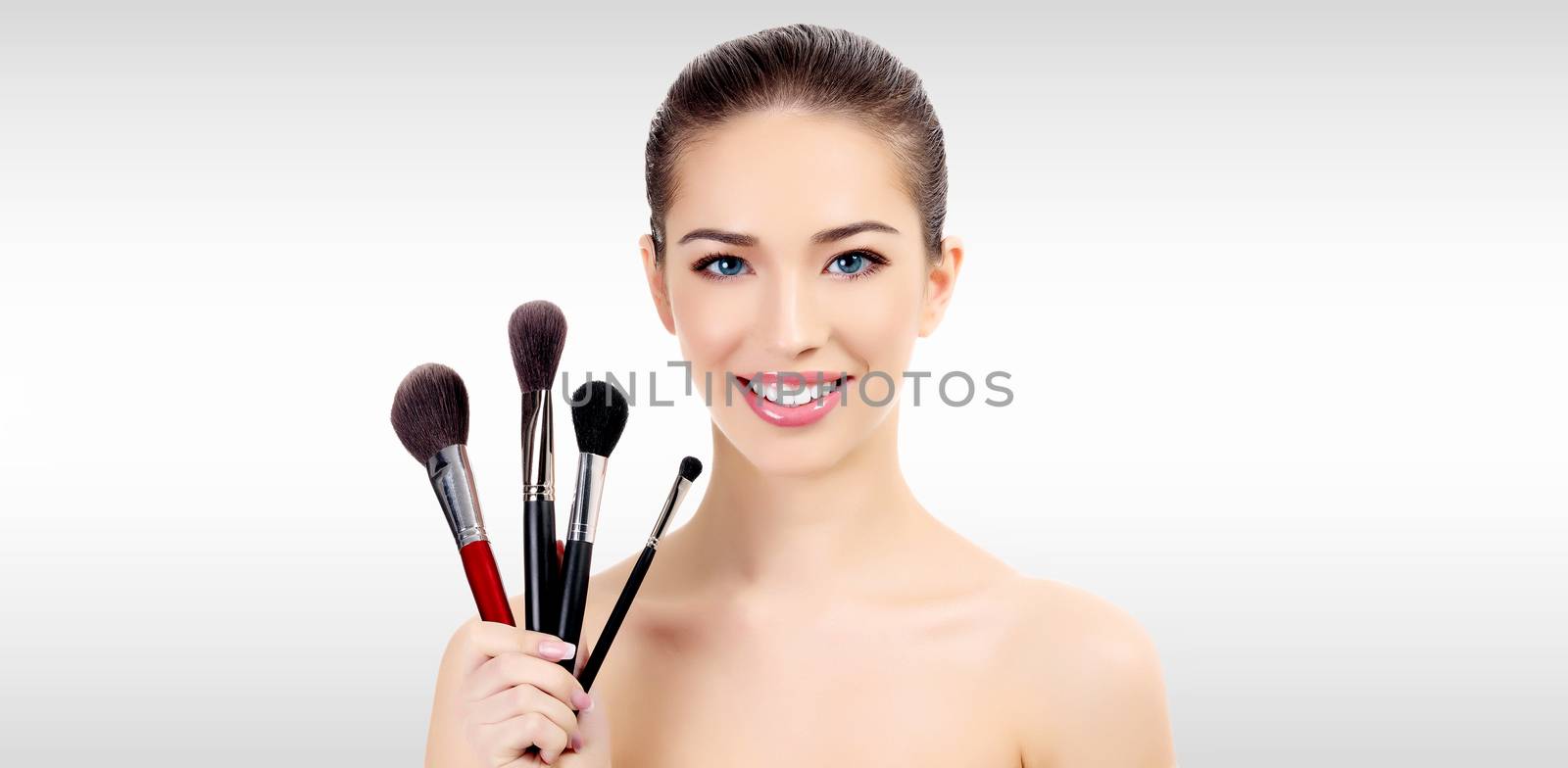 Pretty woman with makeup brushes against a grey background with copyspace