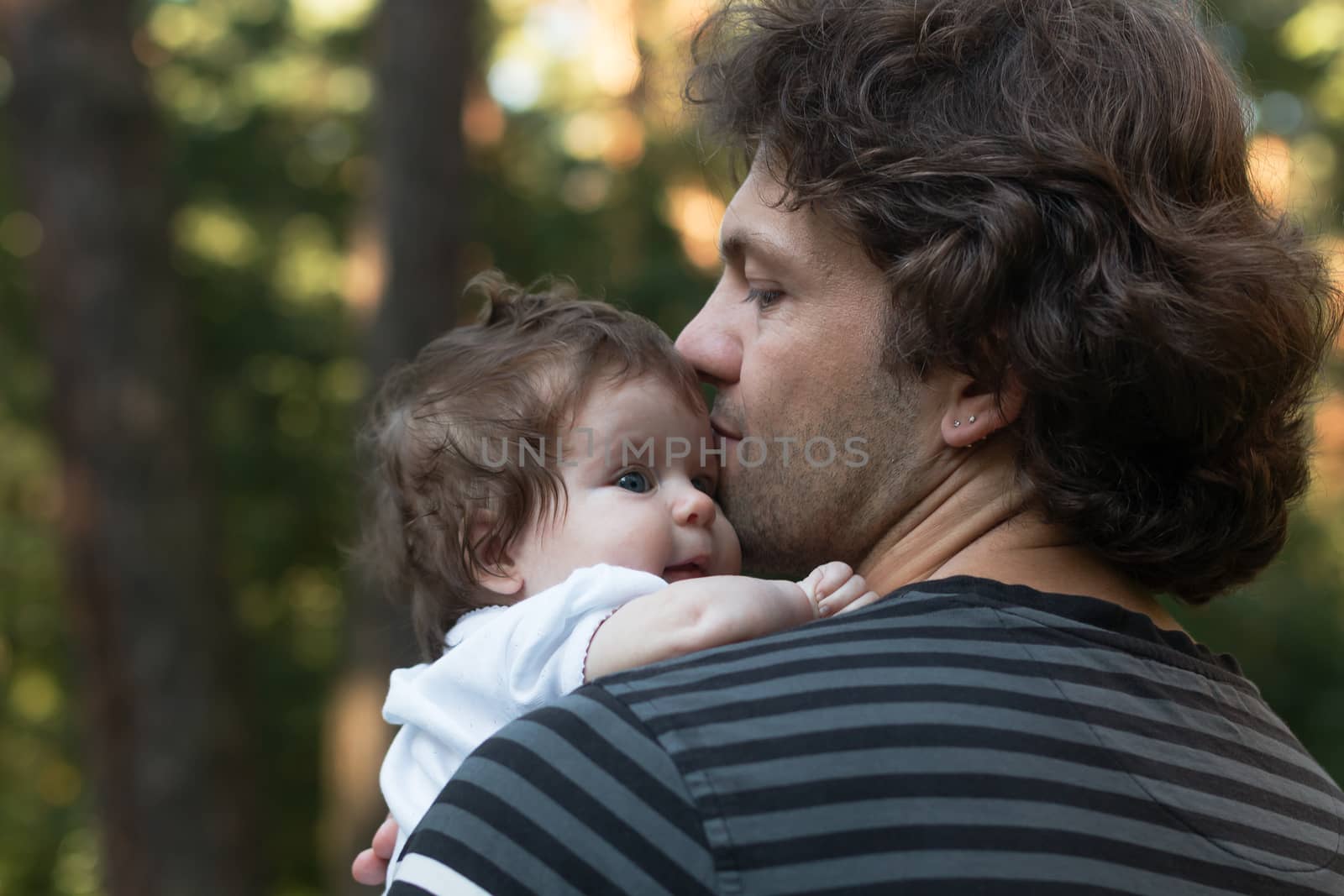 Dad holding his little blue-eyed daughter in his arms for a walk in the park. Summer day, family nature walk, sunny.