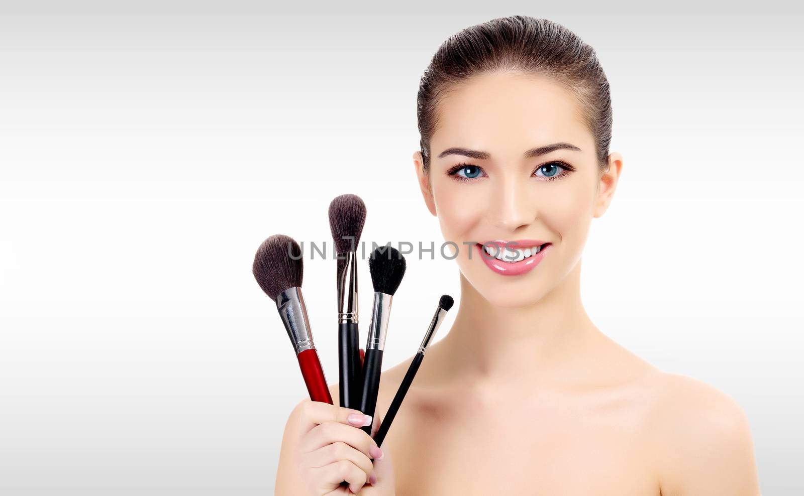 Pretty woman with makeup brushes against a grey background with copyspace