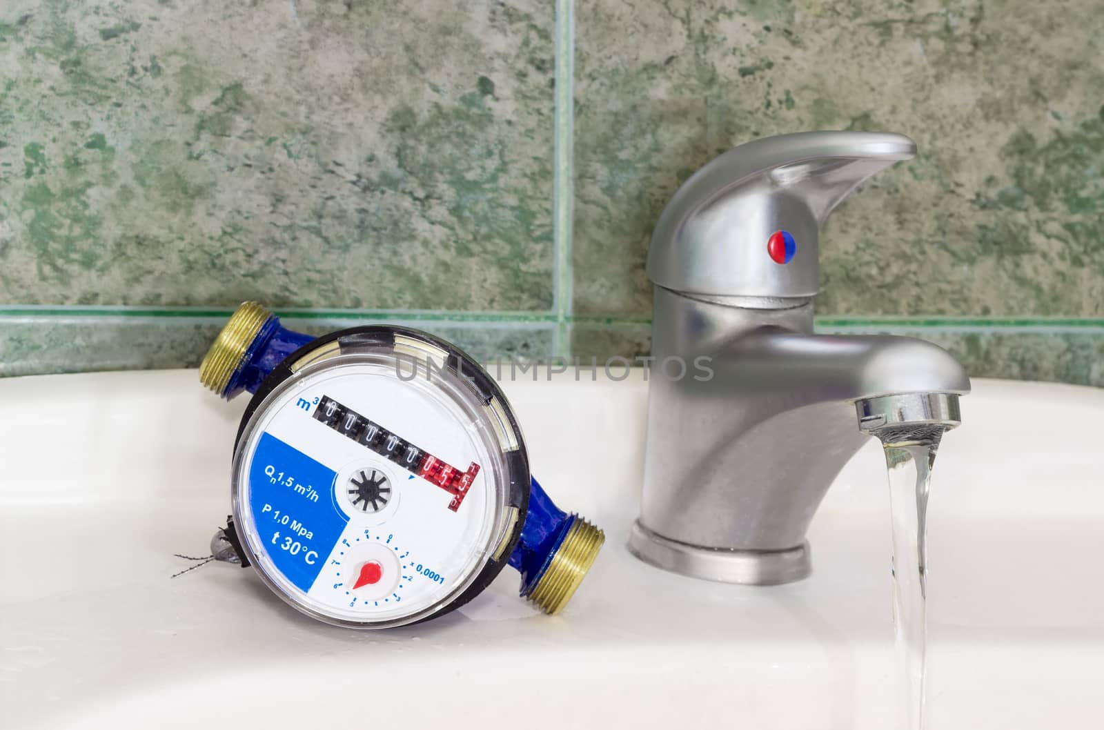 Not connected meter for consumption measuring of a cold water on a wash basin beside mounted handle mixer tap and water flowing from him on background of a wall with green tiles

