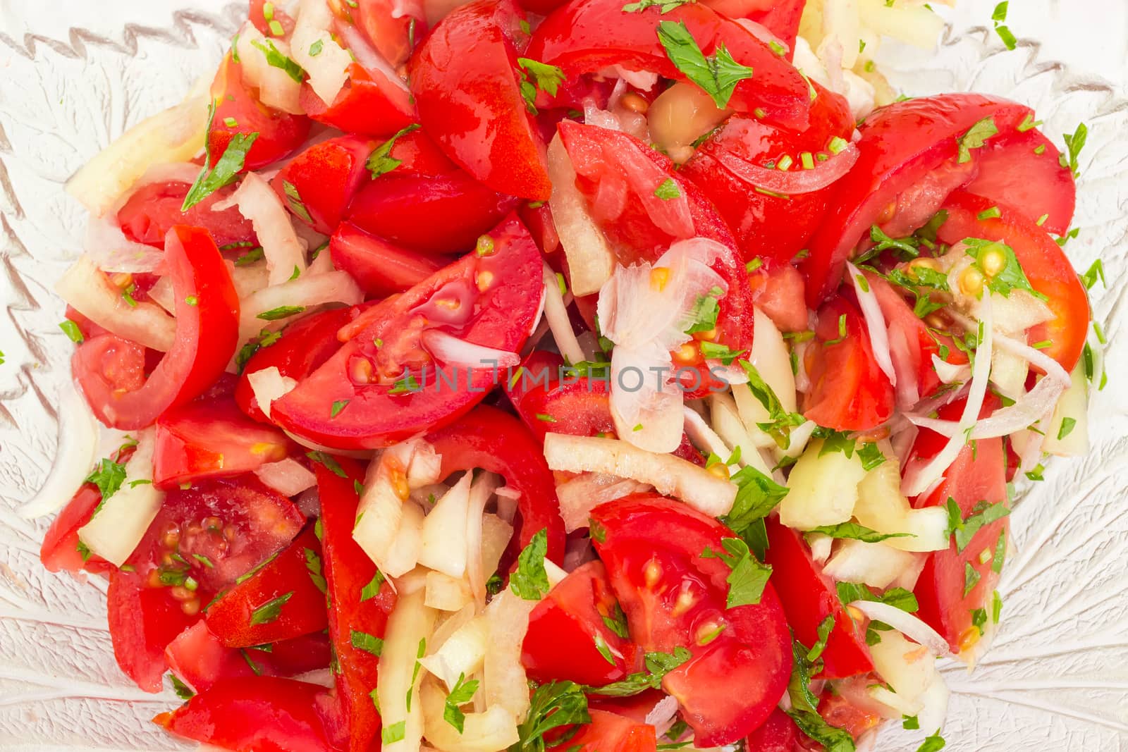 Background of the vegetable salad of a fresh sliced tomatoes, white bell pepper, onion and potherb in a glass salad bowl
