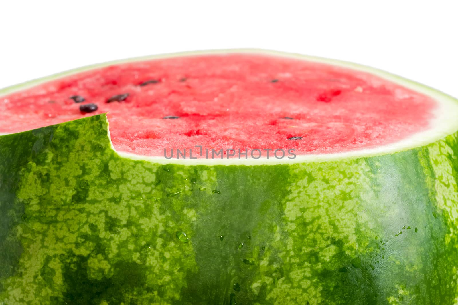 Fragment of the watermelon with green striped rind and deep red flesh with partially cut upper part closeup at shallow depth of field on a white background
