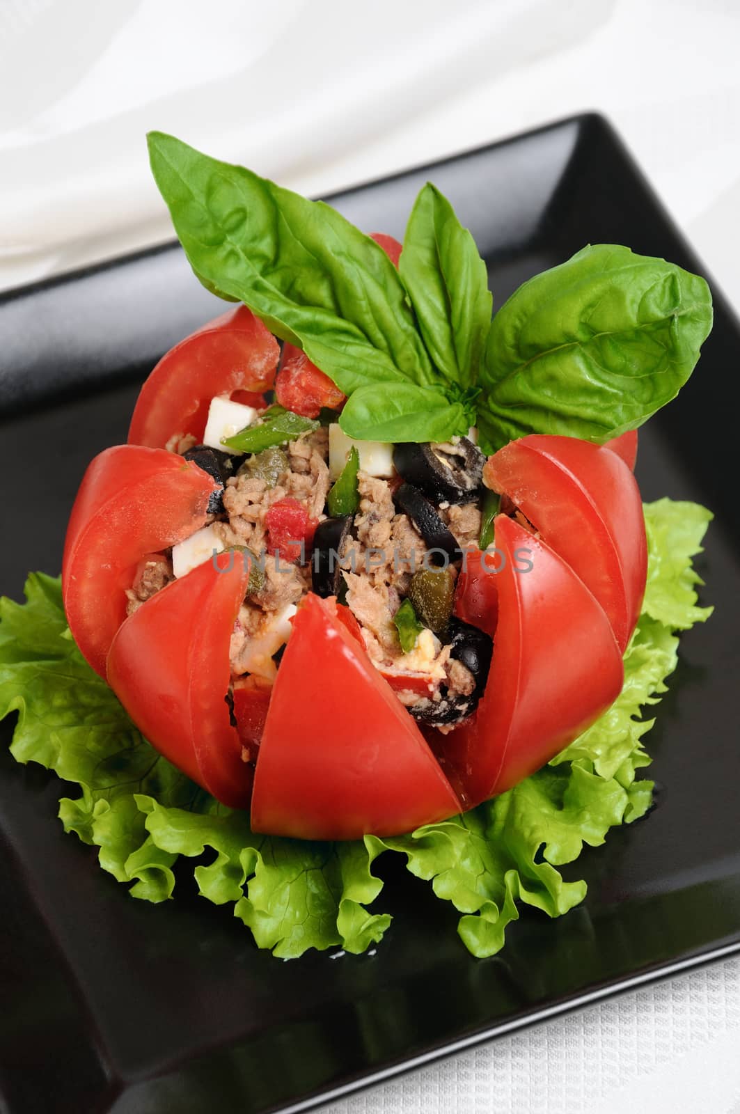 Festive appetizer. Tomato stuffed with chopped tuna salad, egg, tomato cubes, olive slices and the addition of capers, greens