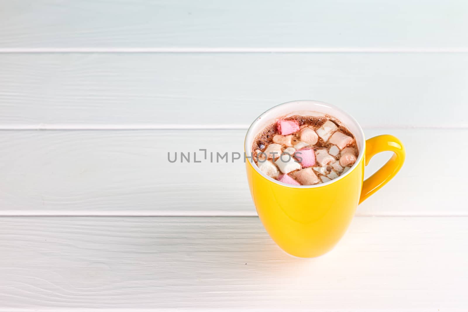 Yellow cup of hot cocoa with marshmallows on white wooden background