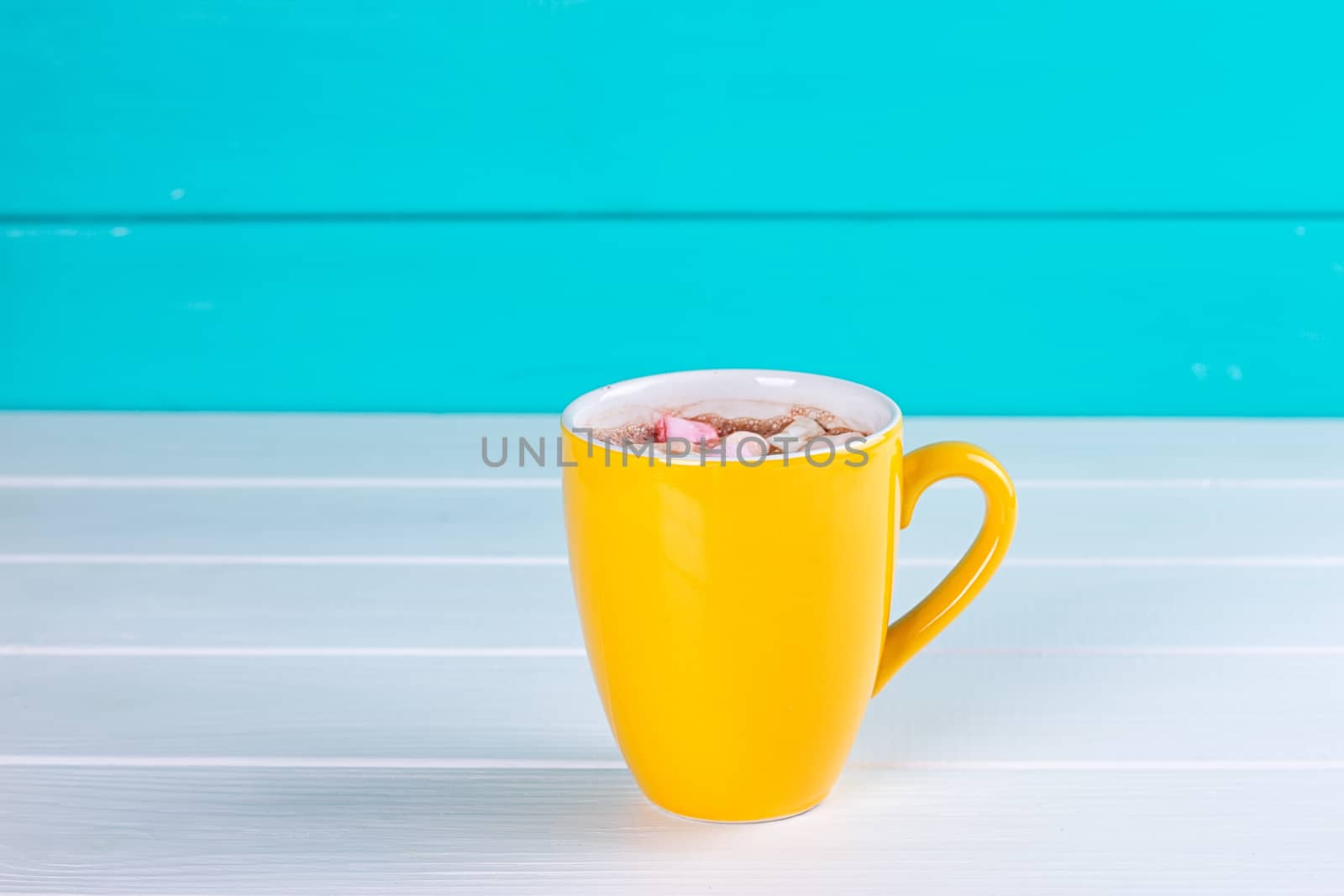 Yellow cup of hot cocoa with marshmallows on blue wooden background