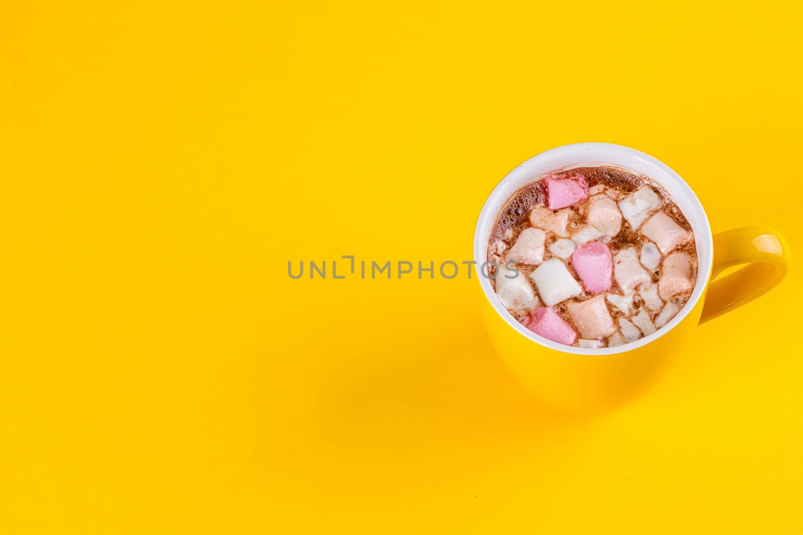 Yellow cup of hot cocoa with marshmallows on yellow background