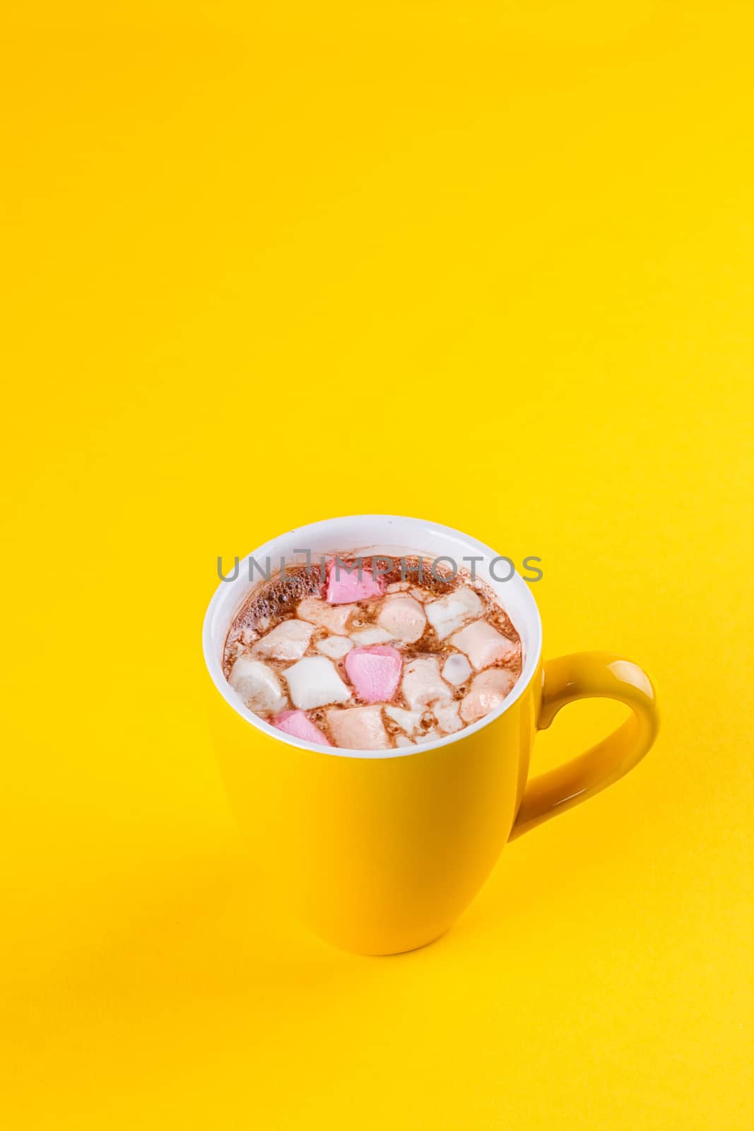Yellow cup of hot cocoa with marshmallows on yellow background