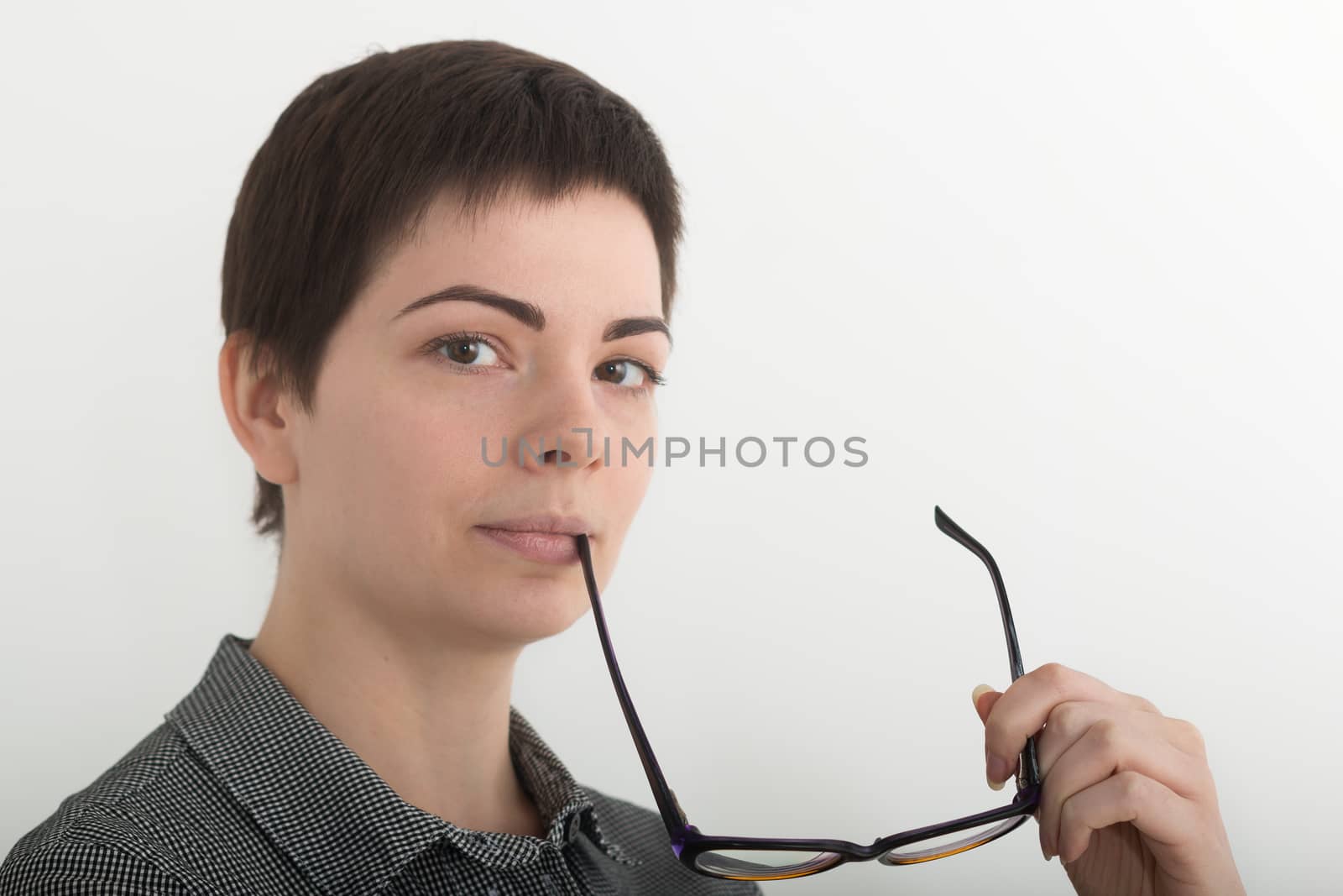 Young attractive girl in black and white plaid shirt seriously holding glasses near her mouth. Isolated on white background, mask included.