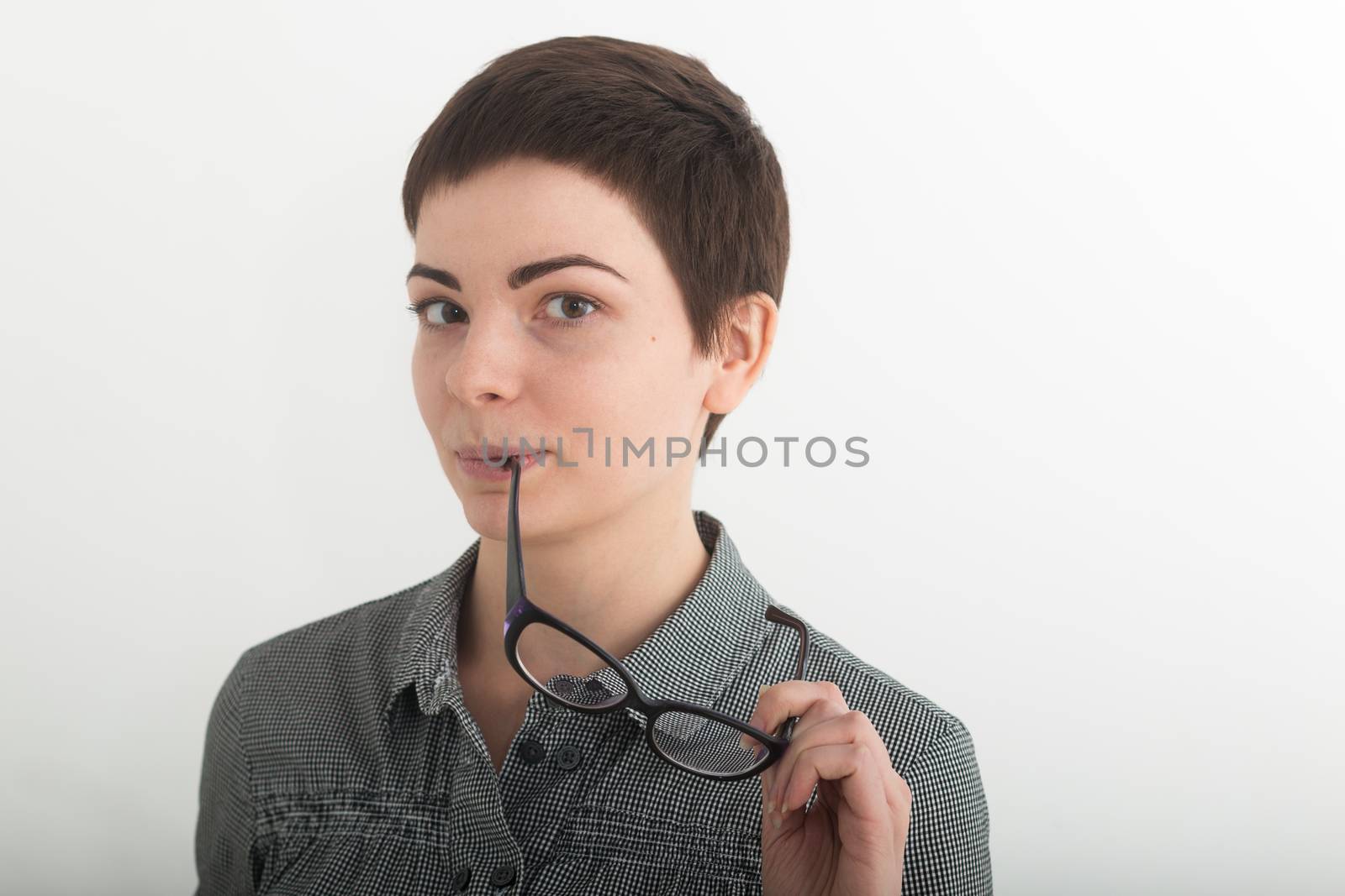 Young attractive girl in black and white plaid shirt seriously holding glasses near her mouth. Isolated on white background, mask included.