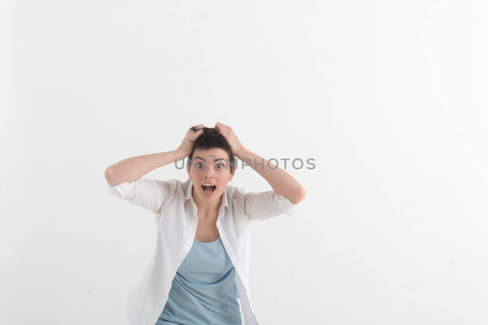 Young woman screaming in terror with hands on her head, mouth wide open looking in panic at the camera. Close up portrait of irritated female shouting, covering her ears, angry with noisy neighbours.
