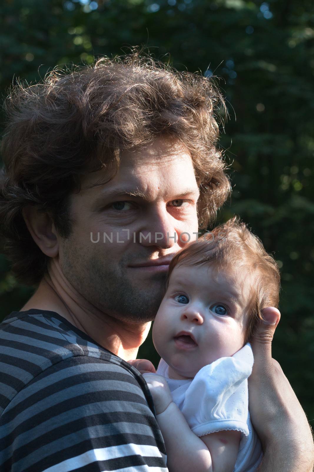 Dad is holding a daughter in his arms for a walk in the park. Spring day, family walk in nature, sunny.