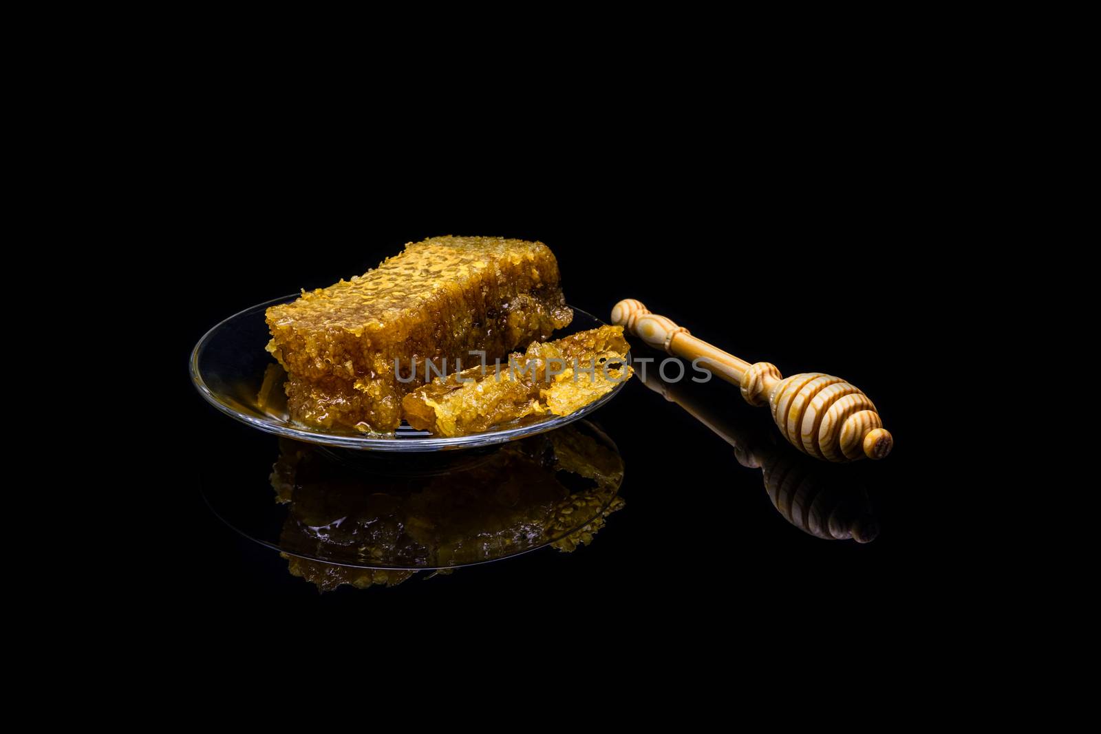 Honey with honeycombs on a glass plate on a black background