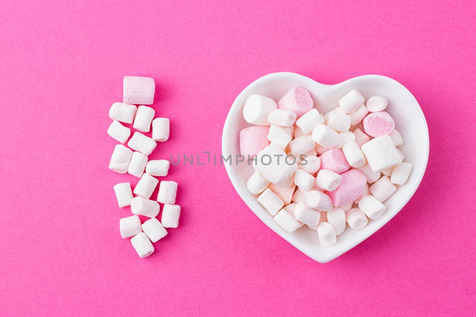 Love concept. Plate in the shape of heart with a marshmallow on a pink background. I love