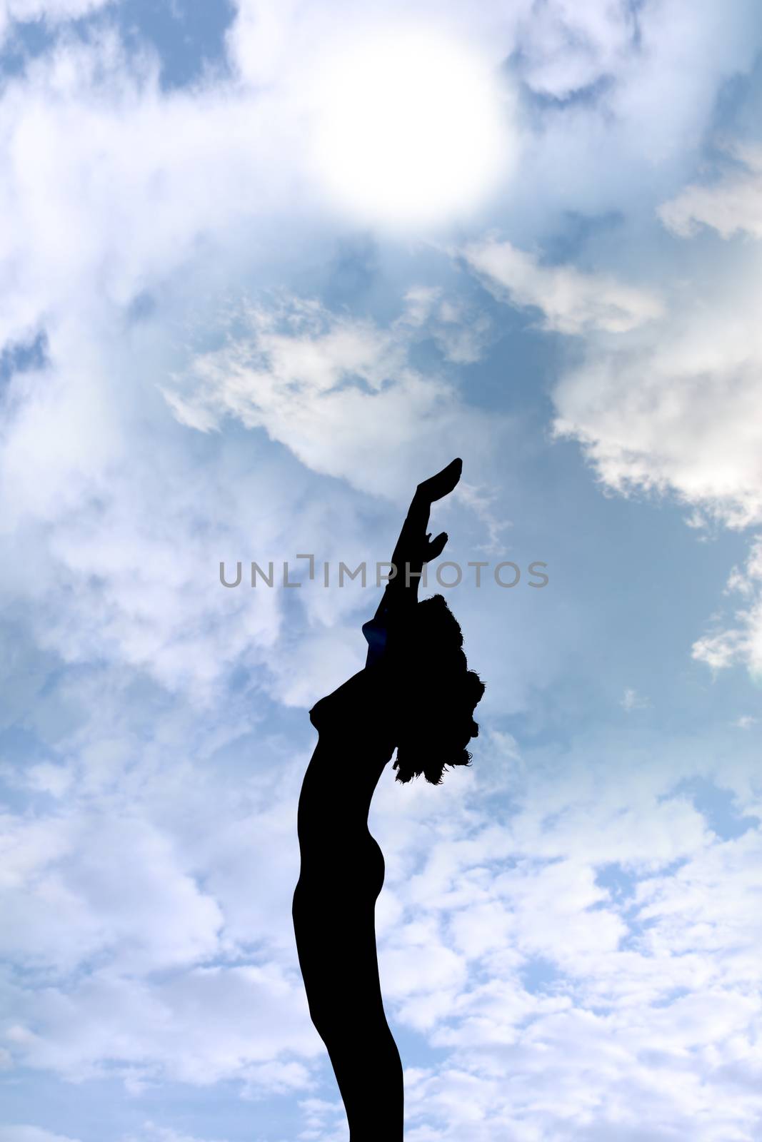 attractive silhouetted nude woman holding her hands up to the sky giving gratitude to the heavens in a yoga pose with a cloudy background