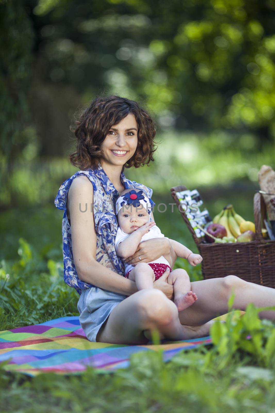 Young beautiful mother sits on blanket with her daughter during a picnic in the park