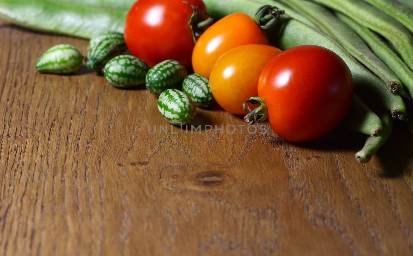 Cucamelons in selective focus with red and orange tomatoes, and green runner beans on wood with copy space