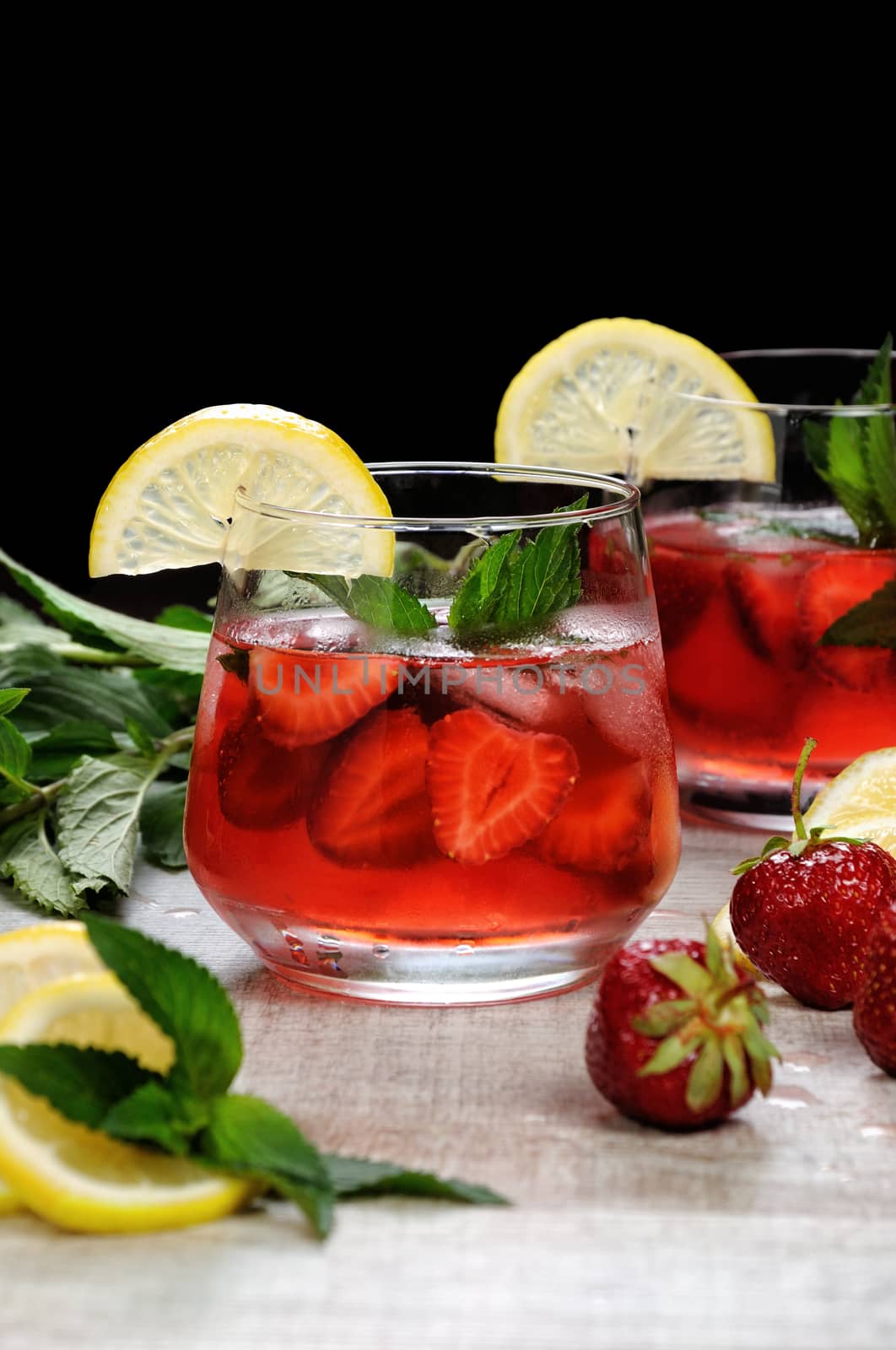 A glass of chilled strawberry lemonade, mint leaves, a slice of lemon with ice