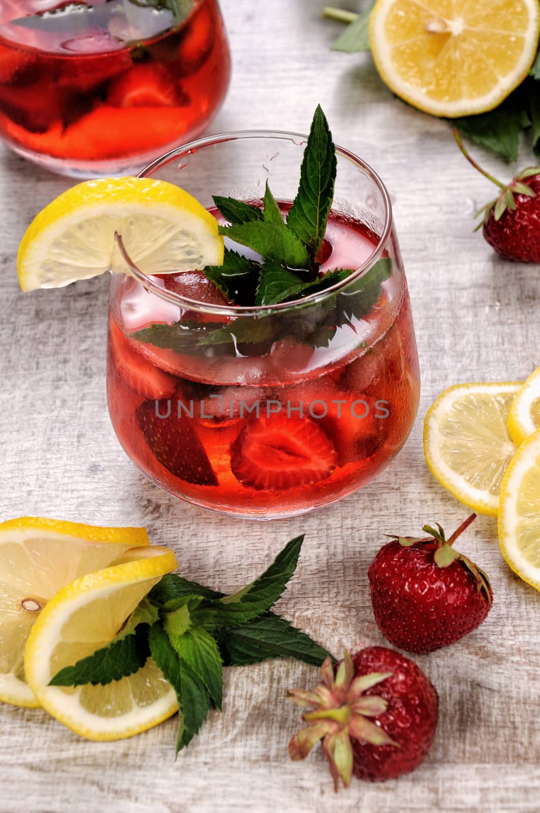 A glass of chilled strawberry lemonade, mint leaves, a slice of lemon with ice