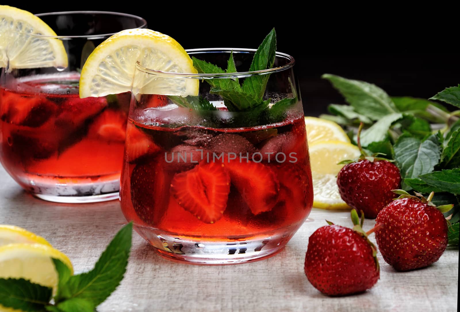 A glass of chilled strawberry lemonade, mint leaves, a slice of lemon with ice