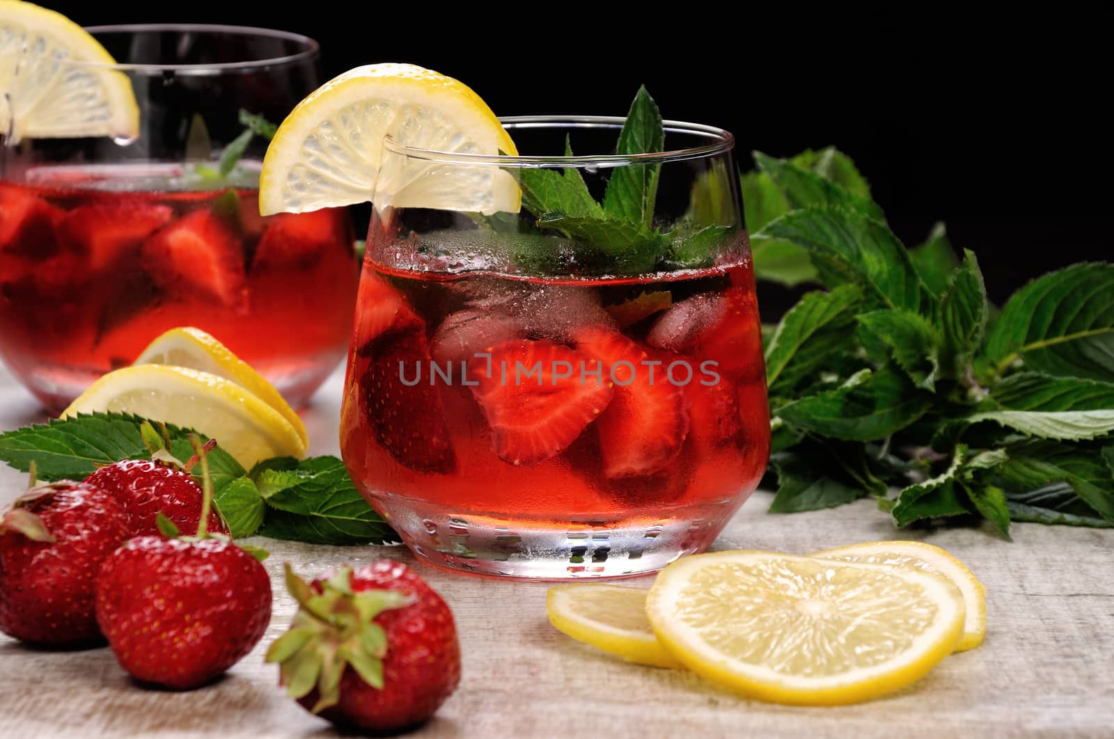 A glass of chilled strawberry lemonade, mint leaves, a slice of lemon with ice