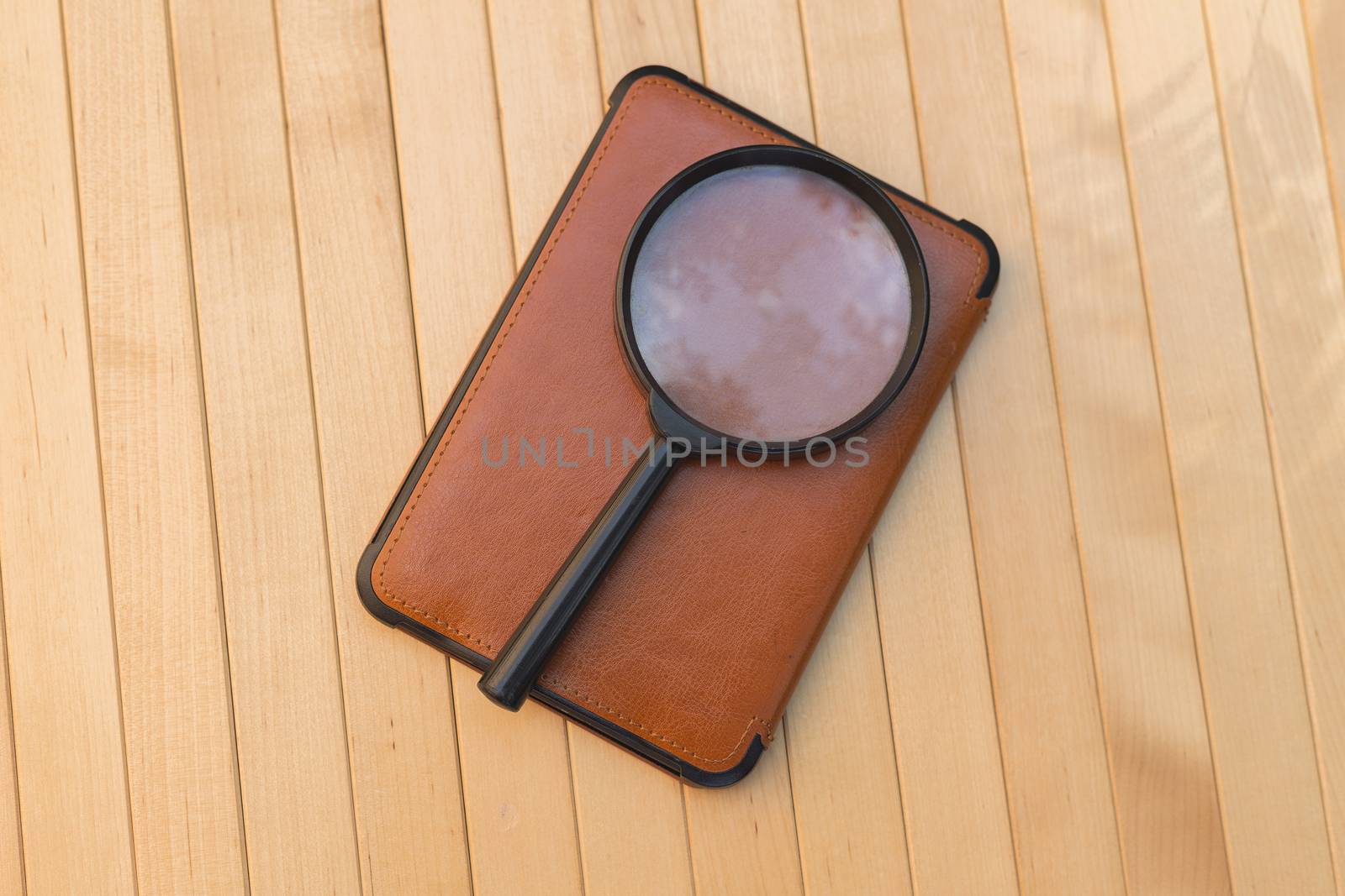 Magnifying glass on e-book on wooden background