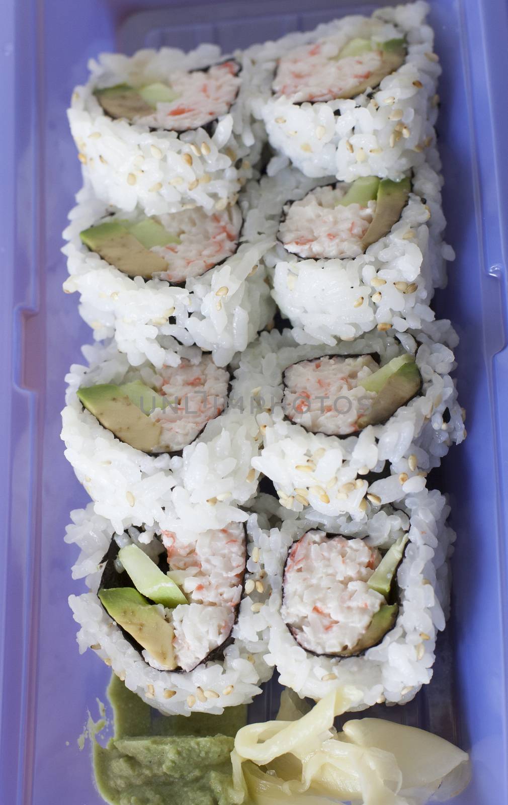 Two rolls of California sushi plated with wasabi sauce and ginger