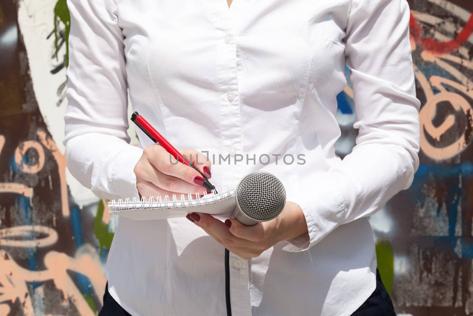 Female reporter at press event, taking notes, holding microphone