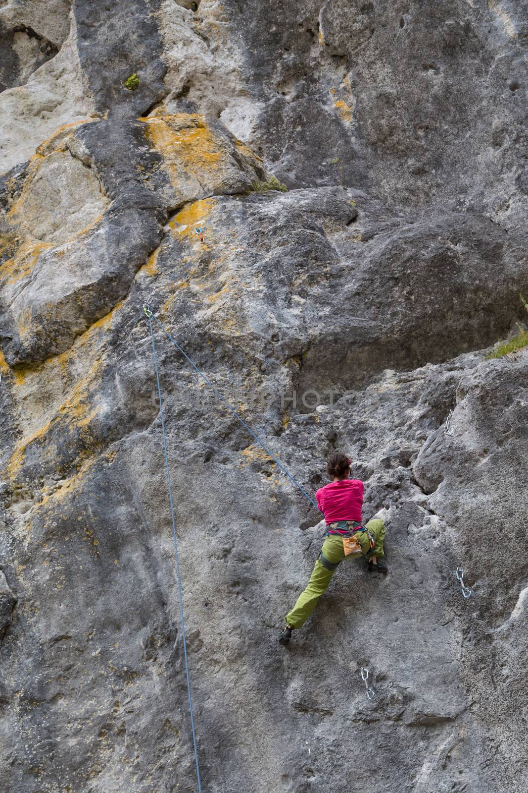 Strong girl climbs on a rock wall, doing sports climbing in nature.