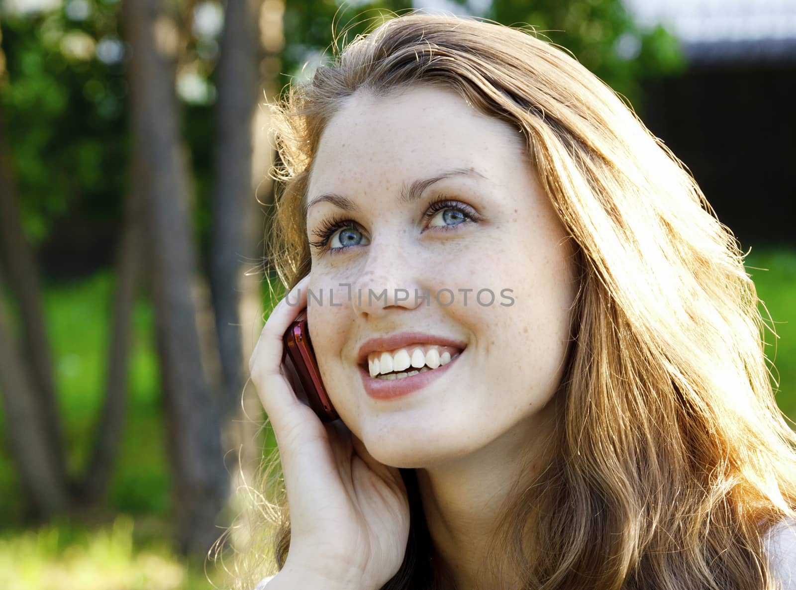 Closeup shot of young smiling woman speaks by a mobile phone by Nobilior