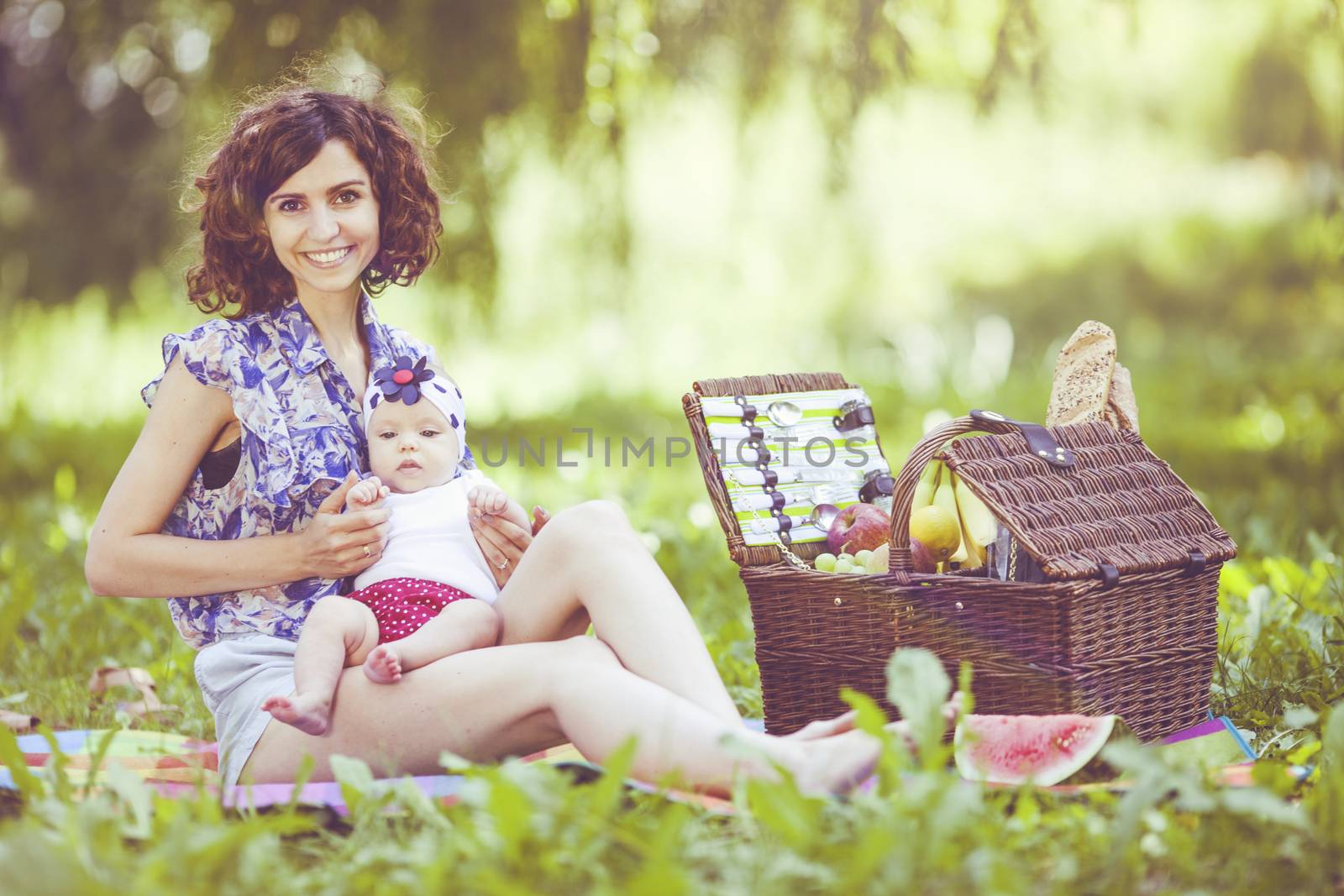 Young beautiful mother sits on blanket with her daughter during a picnic in the park