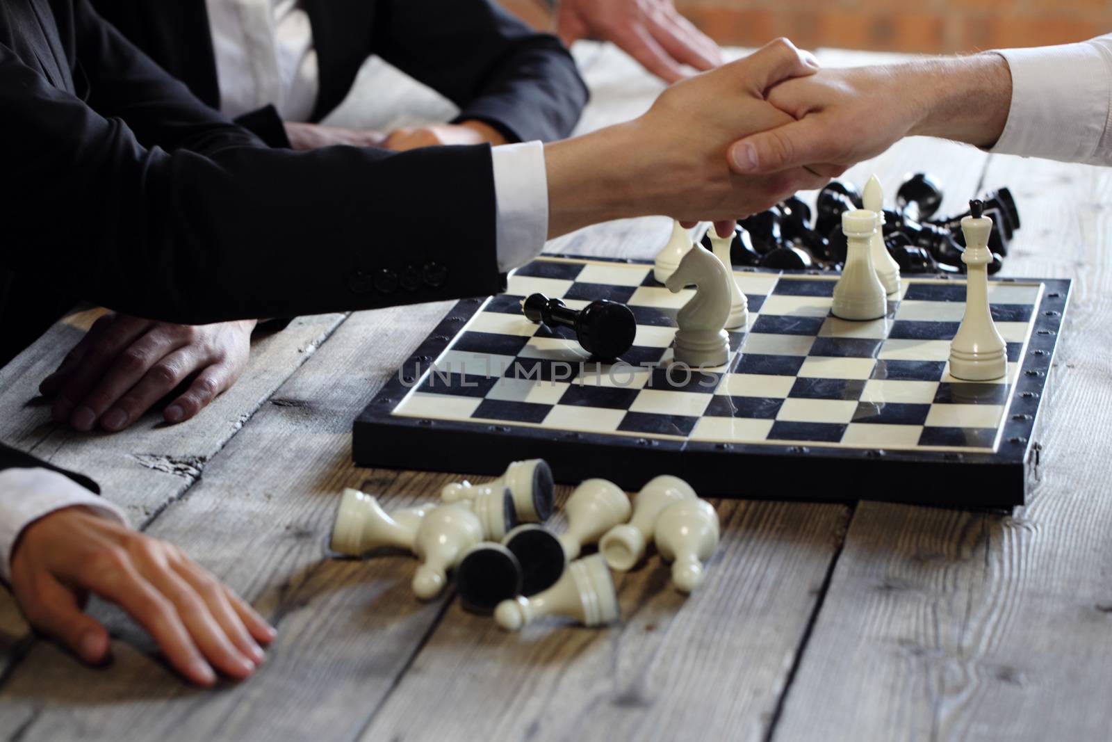 Business people shaking hands over chessboard after the game