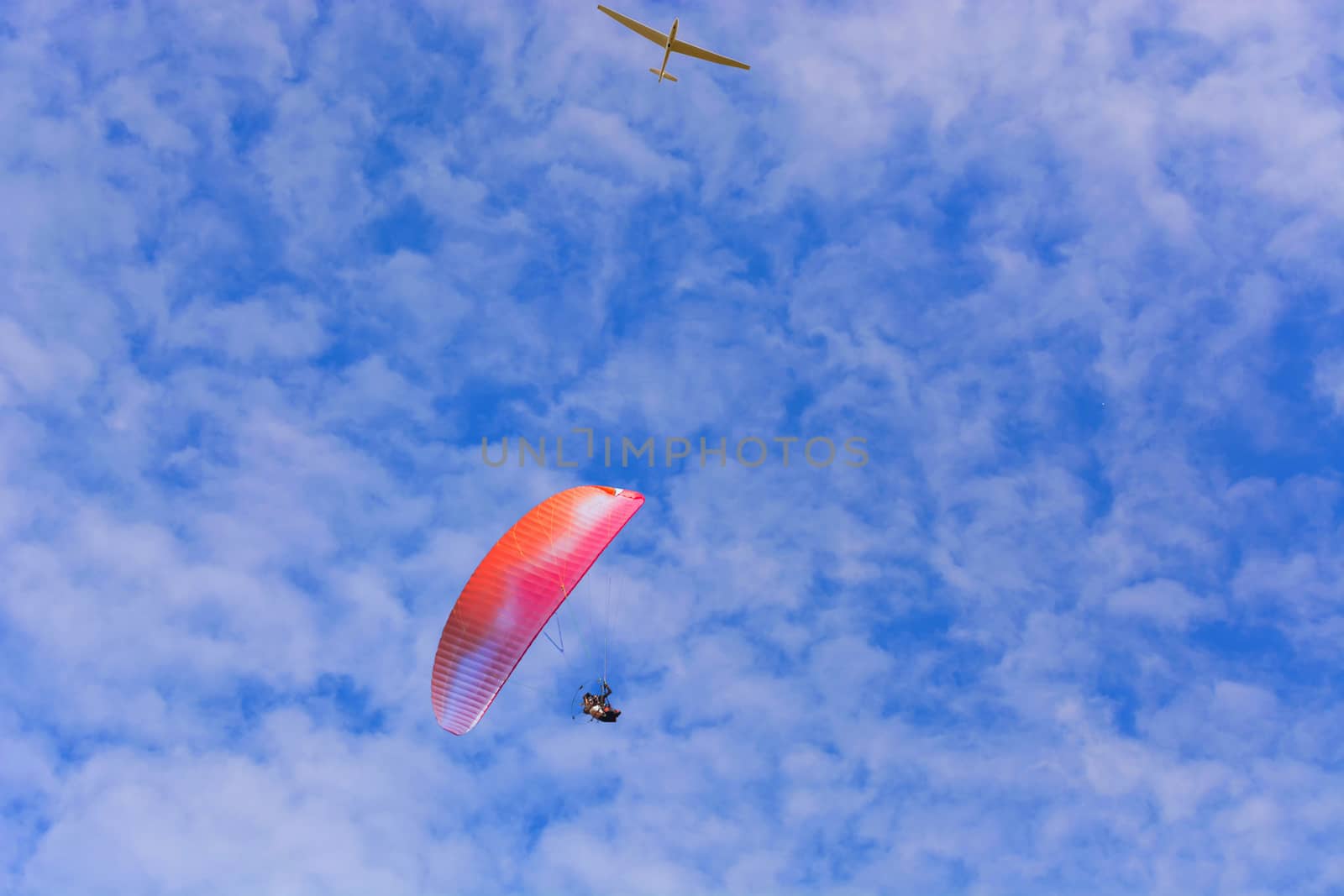 Paramotor wing airman  and motorless flying with a glider against blue sky.
