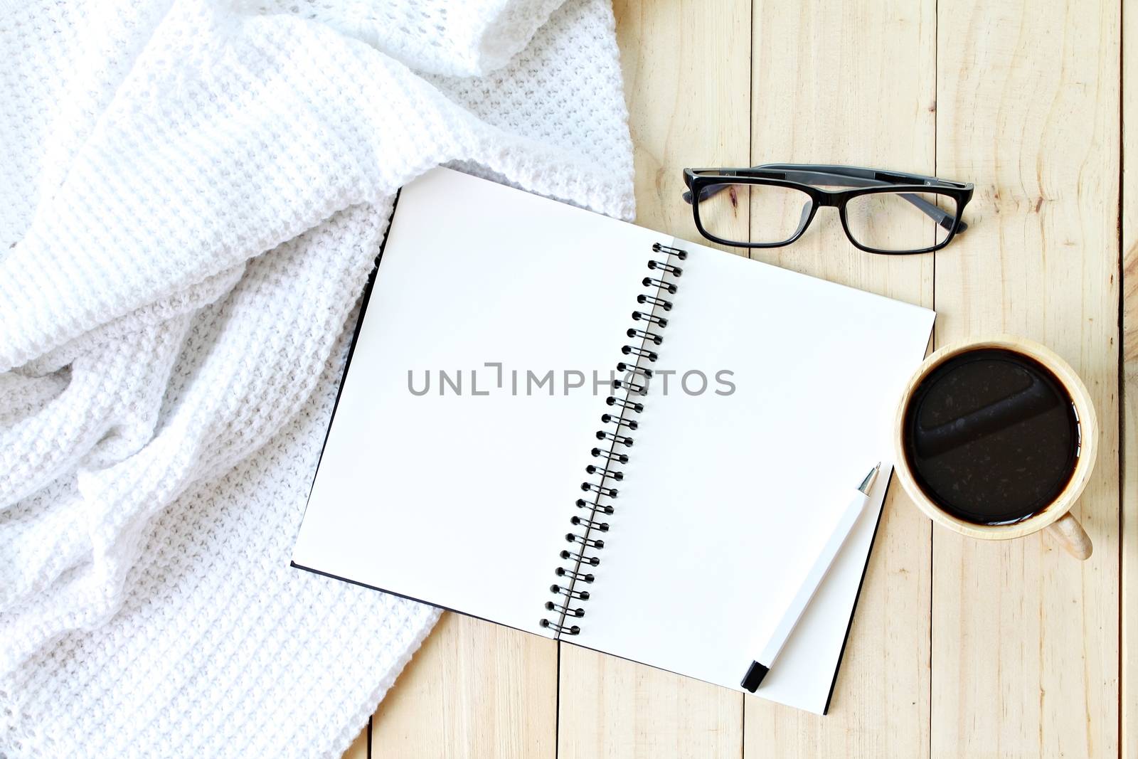 Business, Holiday or weekend concept : Flat lay of white knitted blanket, eyeglasses, cup of coffee and blank notebook paper on wooden background