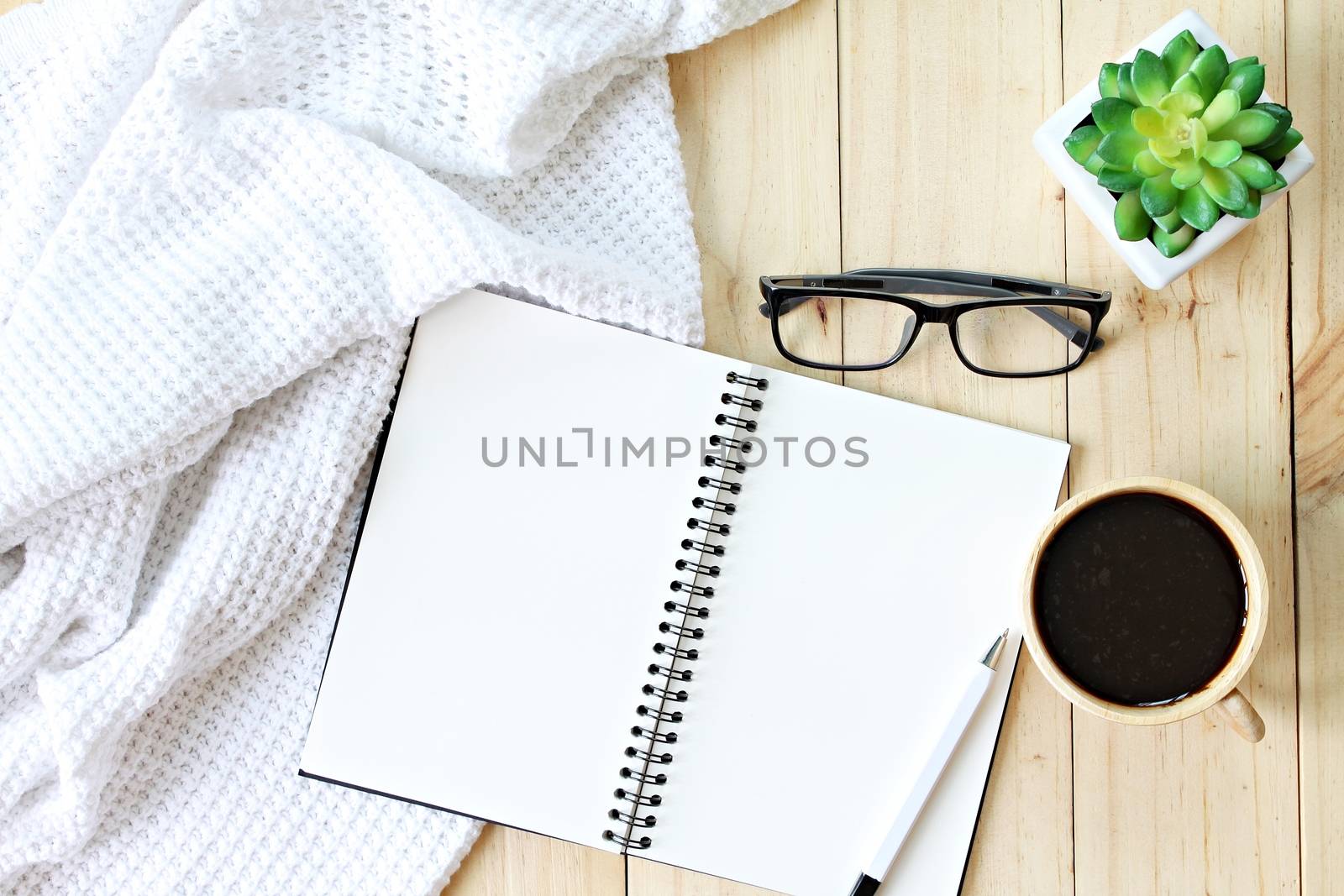 Business, Holiday, weekend or winter concept : Flat lay or top view of white knitted blanket, eyeglasses, cup of coffee and blank notebook paper on wooden background