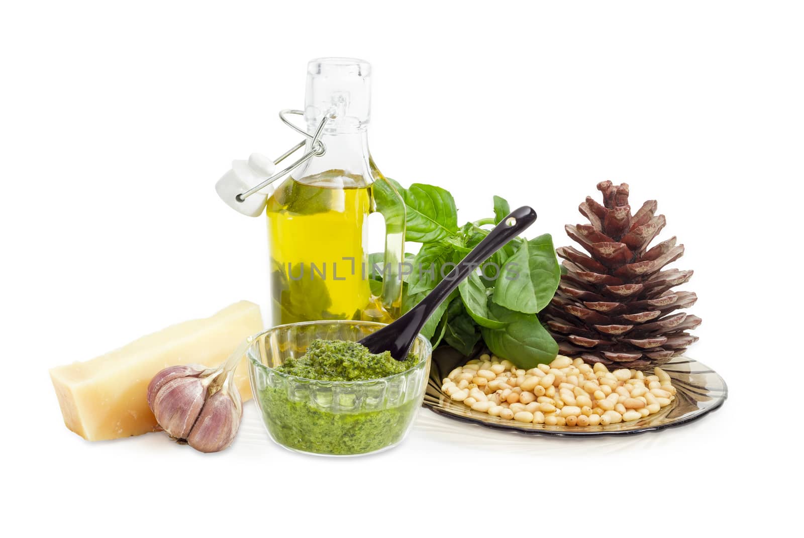 Sauce basil pesto in the small glass bowl on a background of ingredients for its preparation and pine cone on a white background
